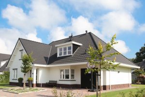 Wit huis met zwarte dakpannen en een veranda.