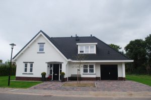 Wit huis met zwarte dakpannen en een veranda.