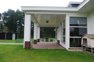 Wit huis met zwarte dakpannen en een veranda.