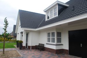 Wit huis met zwarte dakpannen en een veranda.