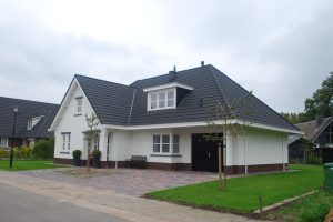Wit huis met zwarte dakpannen en een veranda.