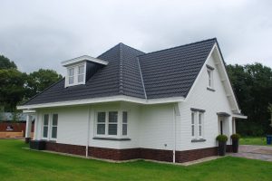 Wit huis met zwarte dakpannen en een veranda.