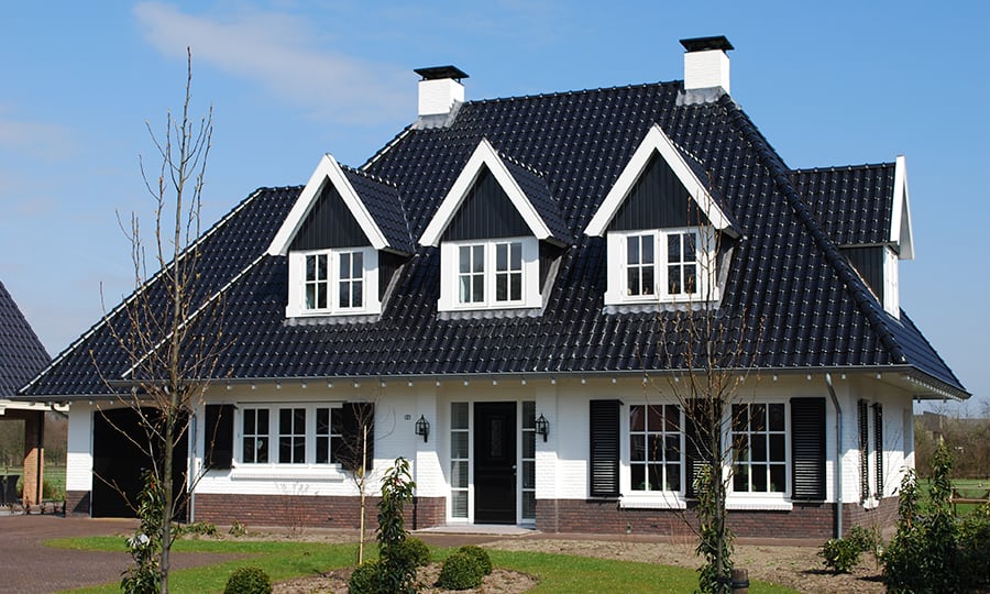 Vrijstaande woning met zwart zadeldak en witte gevel. Drie dakkapellen, grote ramen en goed onderhouden tuin.